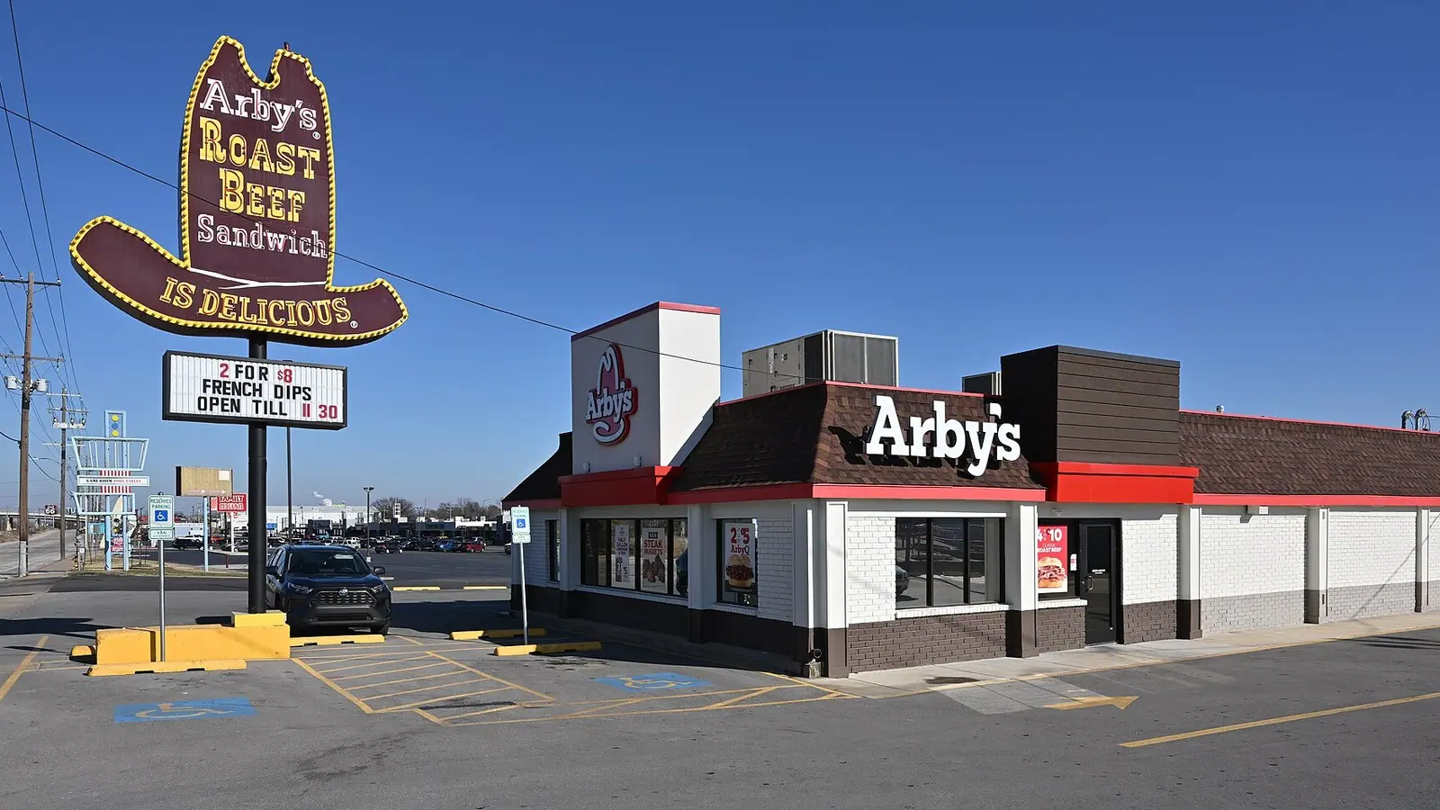 An Arby's restaurant with a red-trimmed brick building and a tall cowboy-hat-shaped Arby's Roast Beef Sandwich sign under a clear blue sky