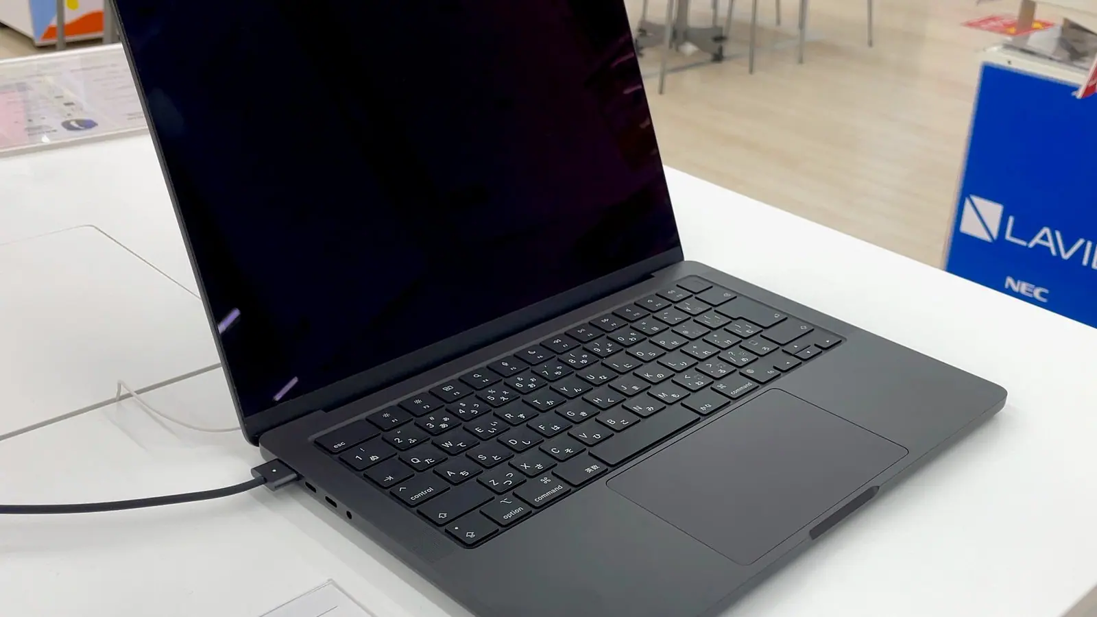 An earlier-generation 14-inch MacBook Pro in space gray open on a white store display table