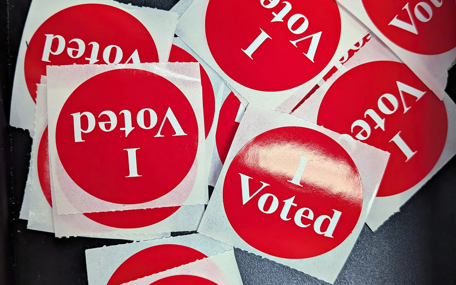 A scattered pile of red and white I Voted stickers at a polling station