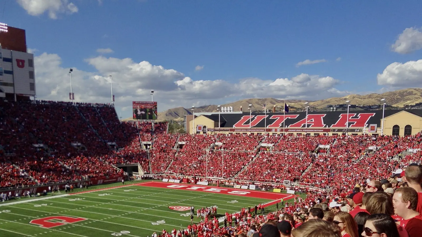 Fans in red fill Rice-Eccles Stadium in Salt Lake City during a Utah Utes football game, with mountains behind the stands