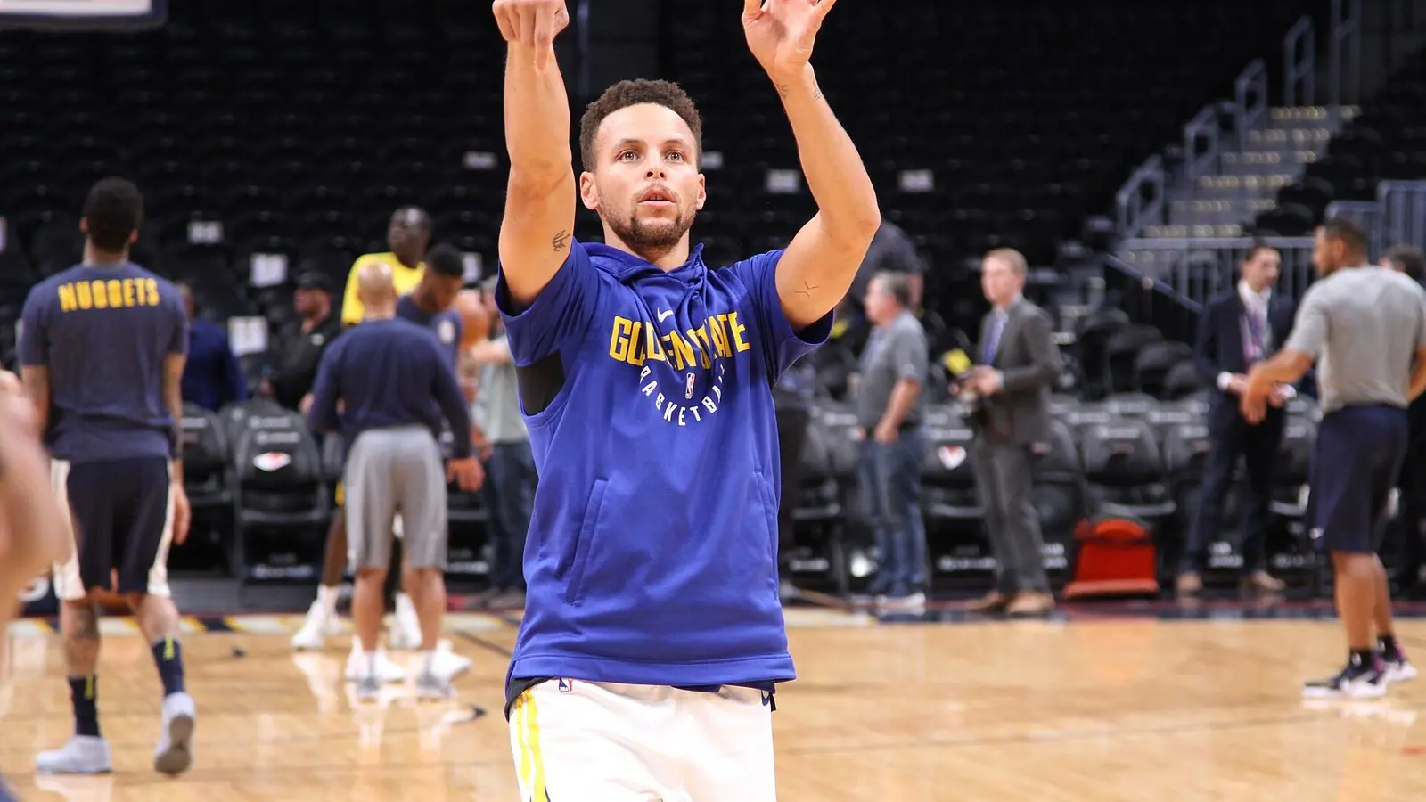Stephen Curry in a blue Golden State warmup shirt follows through on a practice jump shot on an NBA court before a game